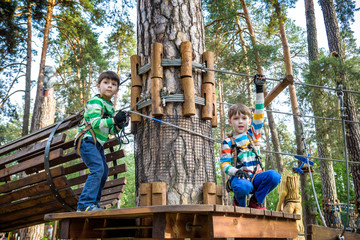 Two little boy boys kid in a helmet and with a safety carbine goes on a rope on the background of forest and sky. Healthy games outdoor