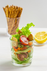 salad in transparent glass tomatoes cucumbers snacks croutons lettuce. Crispas and lemon in the background. salad dressing with lemon dressing, vertical