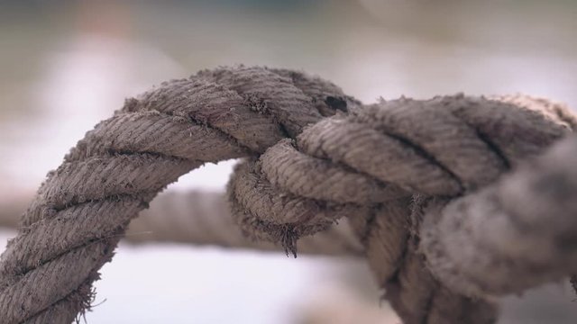 large knot on old brown ship rope over calm water connected with wooden fishing boat closeup
