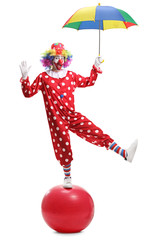 Funny clown holding an umbrella and standing on a giant ball