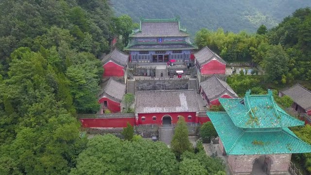 Front view to watchtower and Main Hall facade of Nanyan Palace at Wudang Shan. Reddish walls, greens tiles combined in a natural park with high density forest. Hubei province, China.