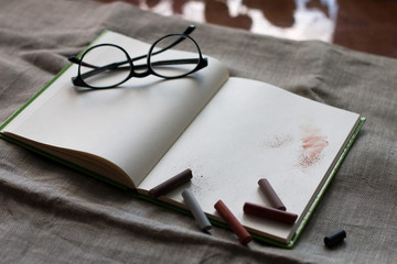 black glasses on the clean white pages of notebook for sketch paint and drawings with pastel on it on the flax background on the table near the window