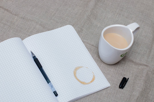 refiner from a cup of coffee on the notebook with open gel pen and cup of milk cofee on the flax backgruond on the table