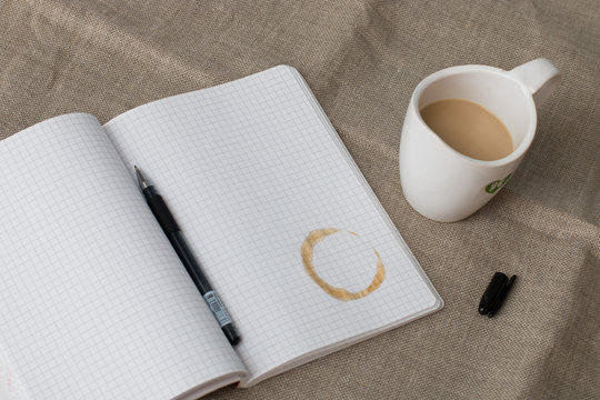 refiner from a cup of coffee on the notebook with open gel pen and cup of milk cofee on the flax backgruond on the table