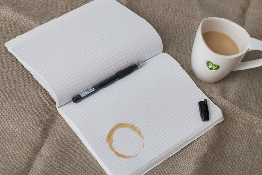 refiner from a cup of coffee on the notebook with open gel pen and cup of milk cofee on the flax backgruond on the table