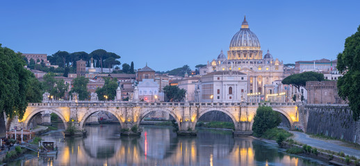 View to bridge with river and Cathedral of Saint Peter in Rome in twilight lights in Italy