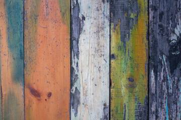 old gray wooden wall fence of multi-colored boards with peeling white, green and red paint. vertical lines. rough surface texture