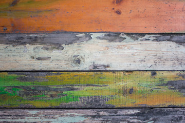 old gray wooden wall fence of multi-colored boards with peeling white, green and red paint. horizontal lines. rough surface texture