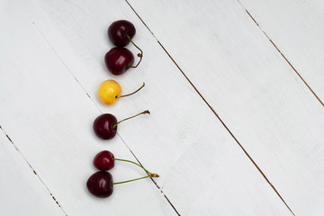 Naklejka na ściany i meble White cherry among red cherries on wooden background. Standing out from the crowd, individuality and difference concept