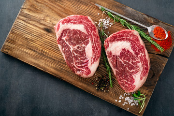 Two raw rib eye steak on the butcher's Board on a wooden table prepared prepared for cooking....