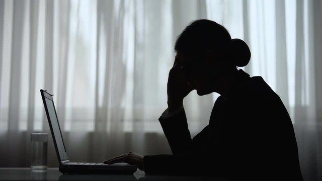 Silhouette of woman taking medicine feeling headache during night work on laptop