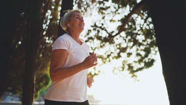 Senior woman is running and listening music. Slow motion