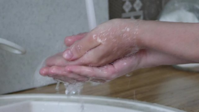 White woman washes her hands under the faucet in the kitchen before cooking