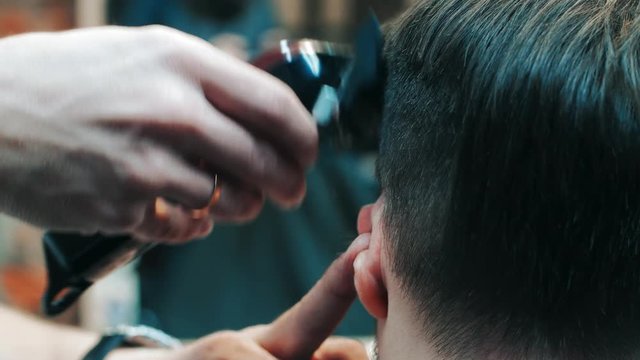 Barber making hairdo to man using electric clipper machine in barbershop