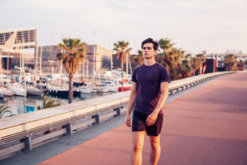 Fototapeta premium Young athletic man running at park with skyscrapers on background. Urban run