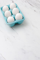 White eggs in turquoise egg tray on white countertop.