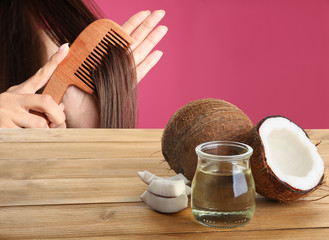 Woman combing her healthy hair and natural coconut oil on wooden table against pink background