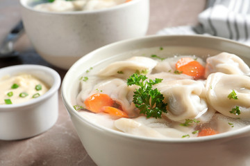 Bowl of tasty dumplings in broth on table, closeup. Space for text