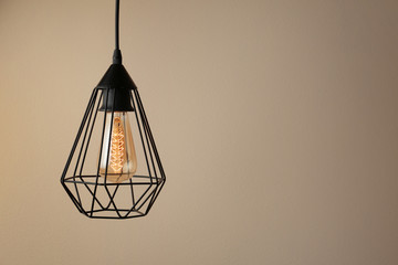 Hanging lamp bulb in chandelier against beige background, space for text