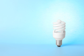 Modern fluorescent lamp bulb on light blue background, space for text