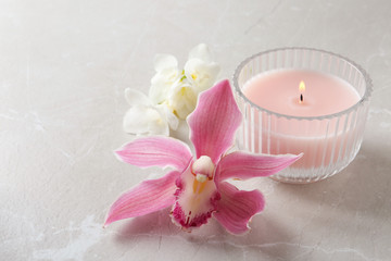 Fototapeta na wymiar Lit candle and beautiful flowers on grey marble table. Space for text