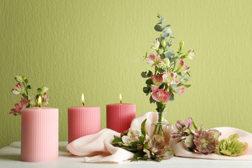 Composition with burning candles and fresh flowers on table near green wall