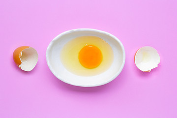 Egg yolk and white in a bowl on pink background.