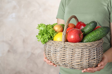Fototapeta premium Woman holding wicker basket with ripe fruits and vegetables on color background, closeup. Space for text