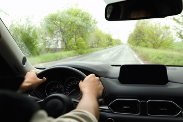 Man driving car on rainy day, closeup of hands