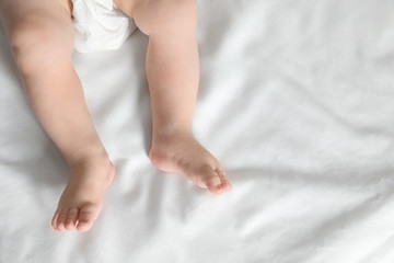 Little baby with cute feet on bed sheet, above view. Space for text