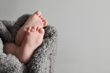 Little baby with cute feet wrapped in soft blanket against grey background, closeup. Space for text