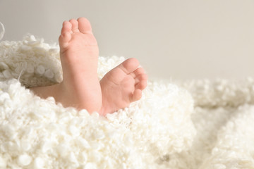 Little baby with cute feet wrapped in soft blanket against light background, closeup. Space for text