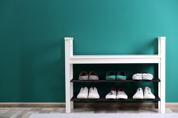 Shoe rack with different footwear near color wall, space for text. Stylish hallway interior