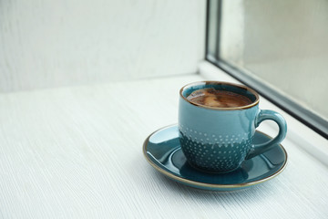 Cup of hot aromatic coffee on white wooden windowsill, space for text. Rainy weather