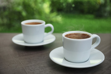 Cups of hot aromatic coffee on brown windowsill, space for text. Rainy weather
