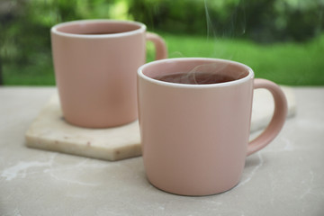 Cups of hot aromatic coffee on white windowsill, closeup. Rainy weather