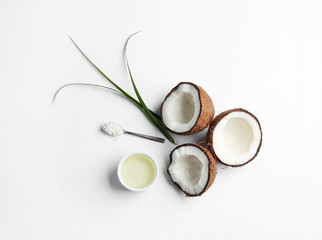 Bowl of natural organic oil and coconuts on white background, top view