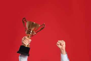 Young man with gold trophy cup on red background, closeup. Space for text