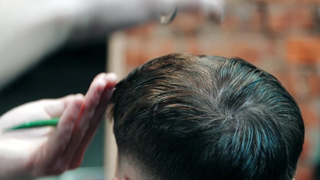 Barber cutting man with scissors under comb. Man having hair cut in barbershop