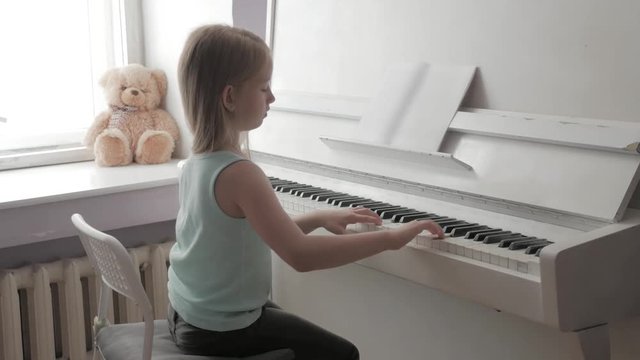 Little girl studying to play the piano at home. Preschool child having fun with learning to play music instrument. Education, skills concept.