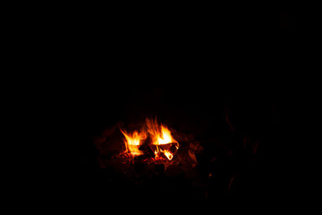 Campfire in the middle of the dark of the night while a sausage is being grilled between the trunks and dry branches from which the flames emerge, photography with natural light