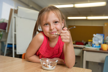 Elementary School Girl Having Granola And Yogurt Snack In Classroom At School