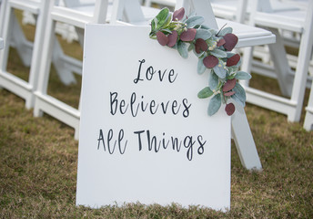 "love believes all things"  white sign in wedding ceremony isle decor
