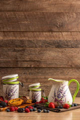 Milk in ceramic jug and two size jars with biscuits and mix of wild berries on wooden background