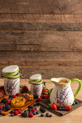 Ceramic jug and two size ceramic jars with cookies and mix of forest fruits on wooden background