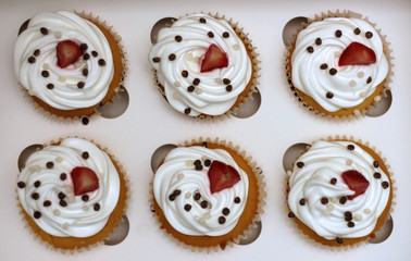 Close-up cupcakes with whipped eggs cream decorated fresh strawberry and chocolate balls in white paper box
