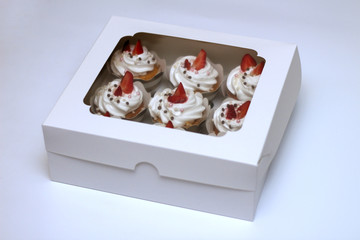 Close-up cupcakes with whipped eggs cream decorated fresh strawberry and chocolate balls in white paper box with transparent cover