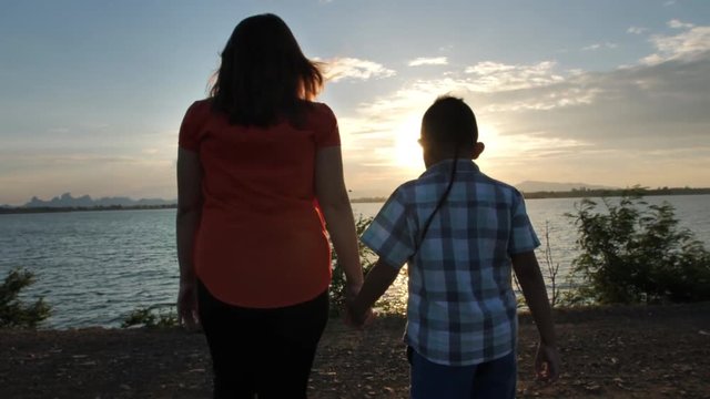 Mother to son, walking hand in hand during the time of sunset. At the river.