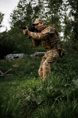 Airsoft soldier in full ammunition with rifle playing strikeball in outdoor in grass