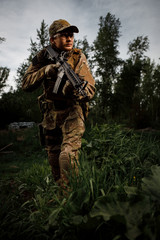 Fototapeta premium Airsoft soldier in full ammunition with rifle playing strikeball in outdoor in grass